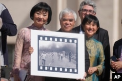 FILE - Pulitzer Prize-winning photographer Nick Ut, center, flanked by Kim Phuc, left, holds his Pulitzer Prize winning photo, as they wait to meet with Pope Francis during the weekly general audience in St. Peter's Square at The Vatican, May 11, 2022.